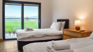 A hotel room with two beds, a nightstand with a lamp, and a large window offering a view of a green landscape. - Acre Luxury Lodges-Cedar Lodge (Walton Presteigne)