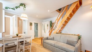 A modern living room with a grey sofa, wooden staircase, and a dining area with white furniture. - GuestReady - Autumn Apartment (Bairro Alto)
