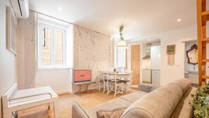 A modern living room with a sofa, a dining table with chairs, a laptop on a small table, and a kitchen area in the background. - GuestReady - Autumn Apartment (Bairro Alto)