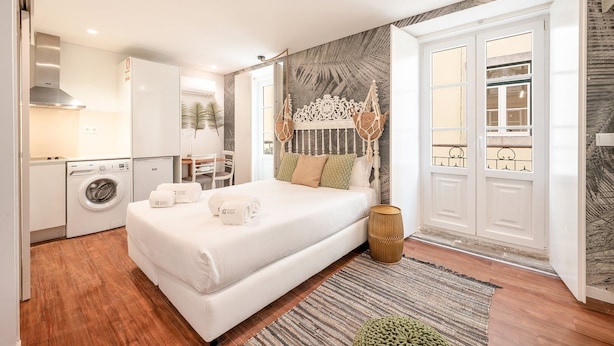 A modern bedroom with a large bed, a washing machine, and a dining area. - GuestReady - Summer Studio (Bairro Alto)