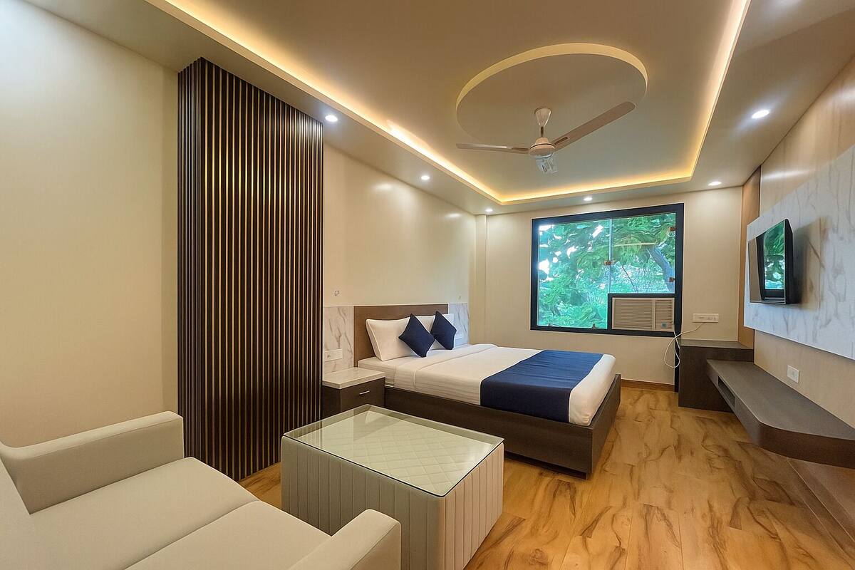 A modern hotel room with a bed, a glass coffee table, a seating area, a TV, and a window with a view of greenery.