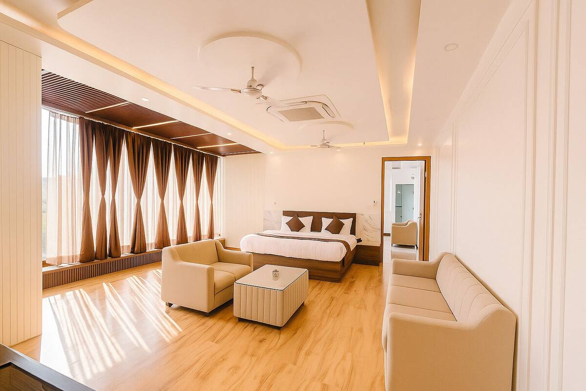 A modern hotel room with a large bed, two sofas, a coffee table, and a ceiling fan.