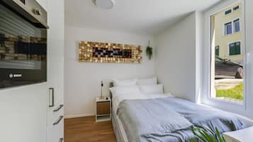 Un dormitorio con una cama, una obra de arte colgada en la pared, una ventana con vistas a un edificio y un electrodoméstico Bosch.