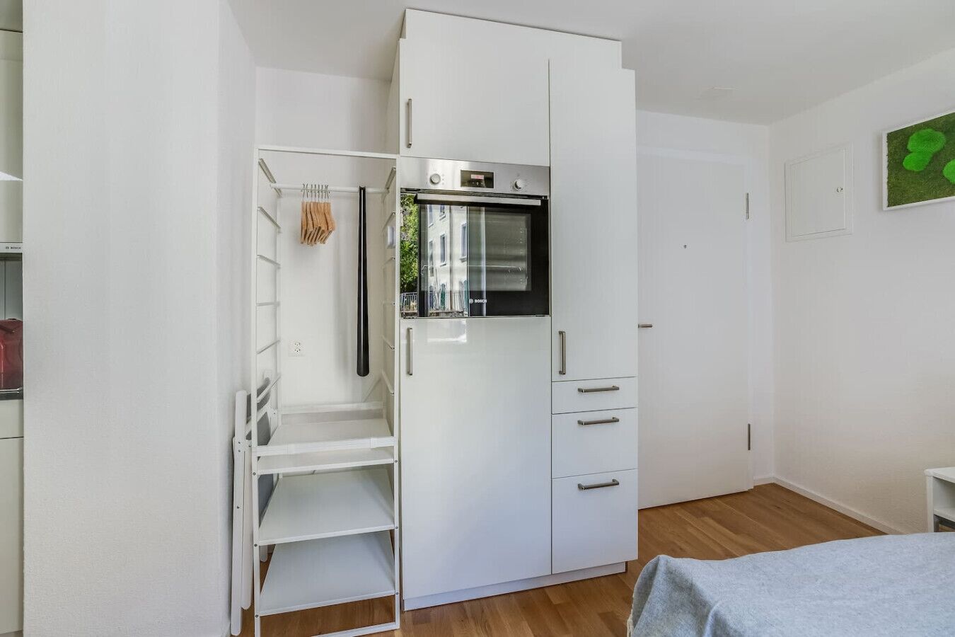 Ein kompakter Raum mit integriertem weißen Kleiderschrank, einer kleinen Küchenzeile mit Mikrowelle und Holzboden.