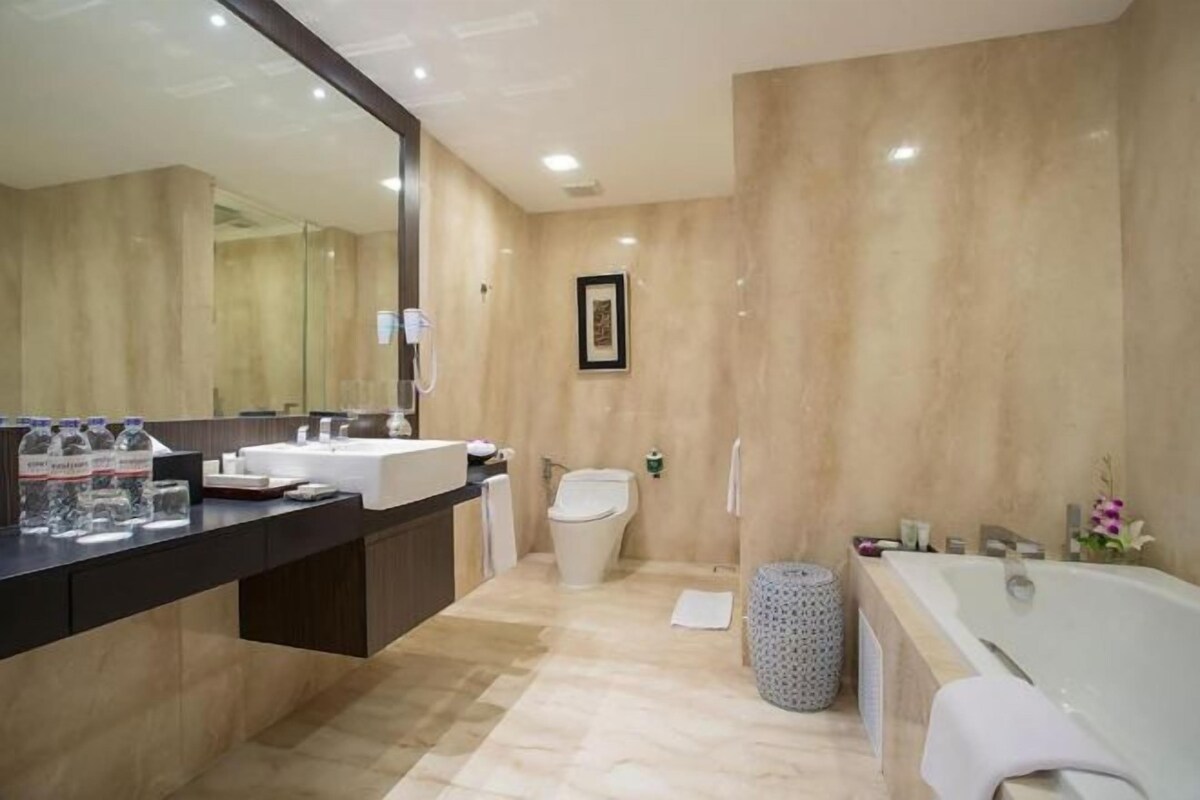 Un baño moderno con un espejo grande, una bañera, un inodoro y un lavamanos.