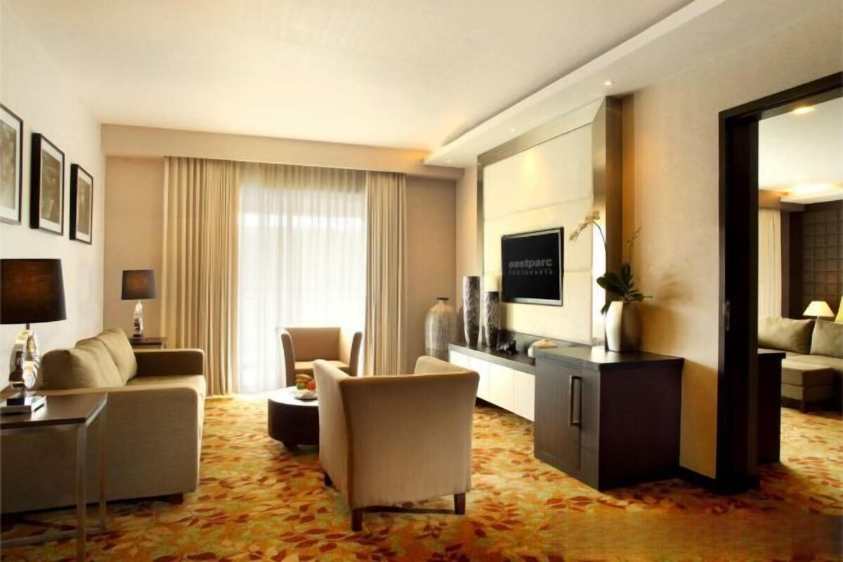 A hotel room with a sofa, armchairs, a TV, a cabinet, and a large mirror.