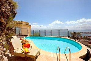 A swimming pool with lounge chairs and a view of the sea.