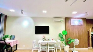 A modern living room with a dining area, a flat-screen TV mounted on the wall, and a wooden panel on one side. - HOMESTAY 2 GIUONG DOI GAN SAN BAY TAN SON NHAT (Thành phố Hồ Chí Minh)