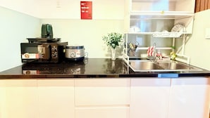 A compact kitchen with a black countertop, a rice cooker, a toaster, and a shelf with dishes. - HOMESTAY 2 GIUONG DOI GAN SAN BAY TAN SON NHAT (Thành phố Hồ Chí Minh)
