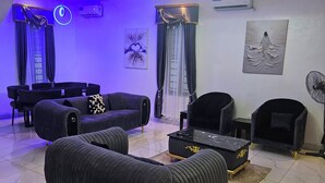 Una sala moderna con candelabro, sofás negros, una mesa de centro y un ventilador.