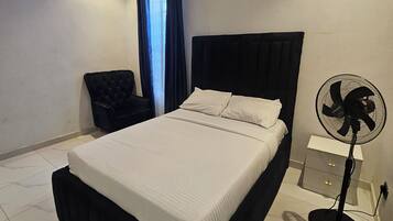 A modern bedroom with a bed, a chair, a nightstand, and a standing fan.