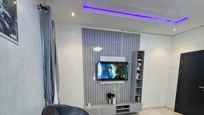 Una sala de estar moderna con un sofá seccional gris, un televisor de pantalla plana montado en una pared gris y una puerta negra a la derecha.