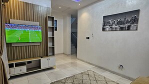 Una sala de estar moderna con un televisor de pantalla plana, un mueble de entretenimiento de madera, un cuadro de paisaje urbano y una alfombra estampada.
