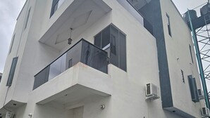 Un edificio moderno de dos pisos con un balcón, una pequeña entrada y un jardín con plantas.