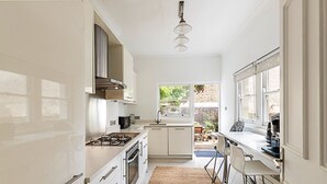Eine moderne Küche mit weißen Schränken, einem Gasherd und einem Fenster mit Blick auf einen Garten.