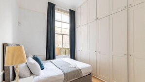 Ein Schlafzimmer mit einem Bett, einem Nachttisch mit Lampe, einem Fenster mit Vorhängen und einem Kleiderschrank.