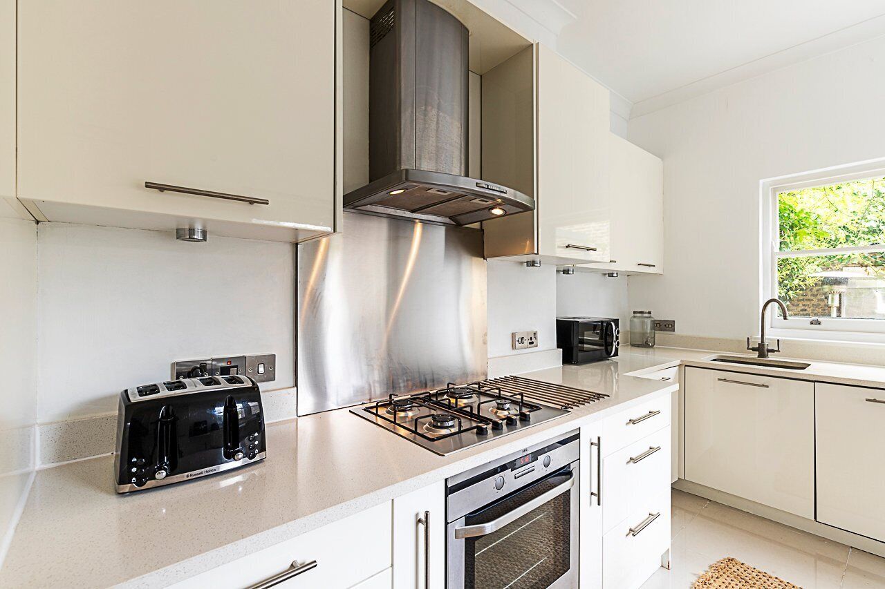 A modern kitchen with stainless steel appliances, a built-in oven, and a window with a view of greenery.