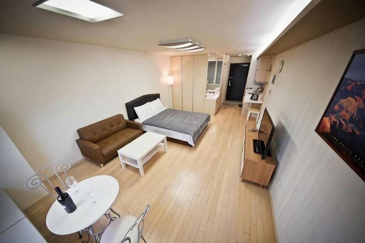 A compact hotel room with a bed, a sofa, a small table, and a TV.