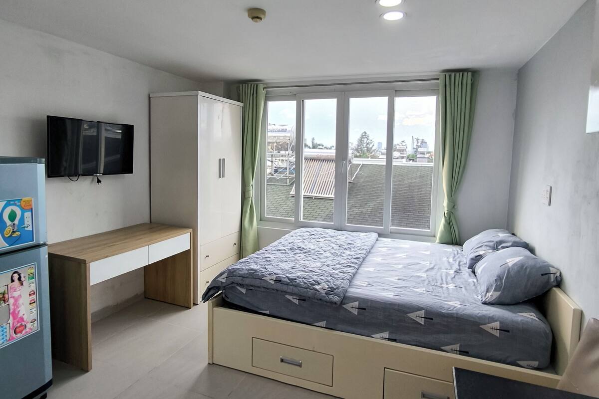 A bedroom with a bed, a desk, a wardrobe, and a television.