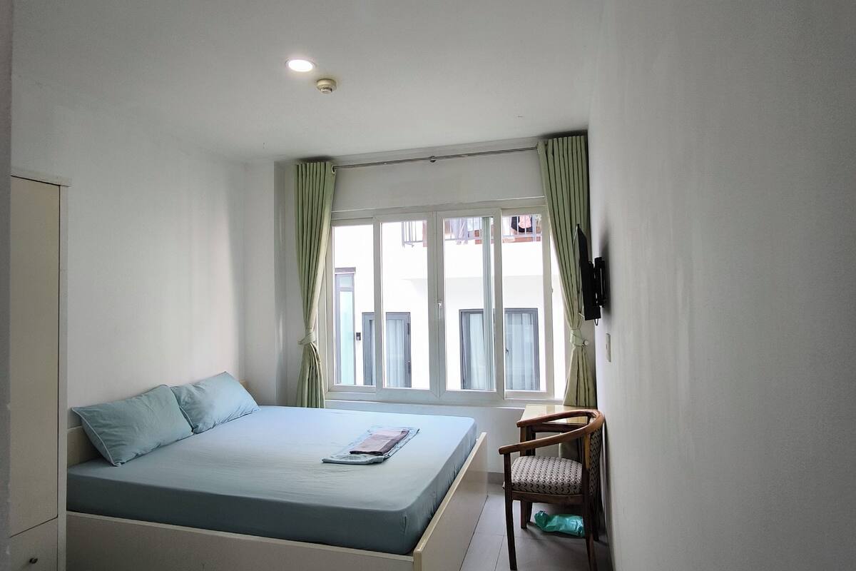 A bedroom with a bed, a chair, a TV, and a window with curtains.