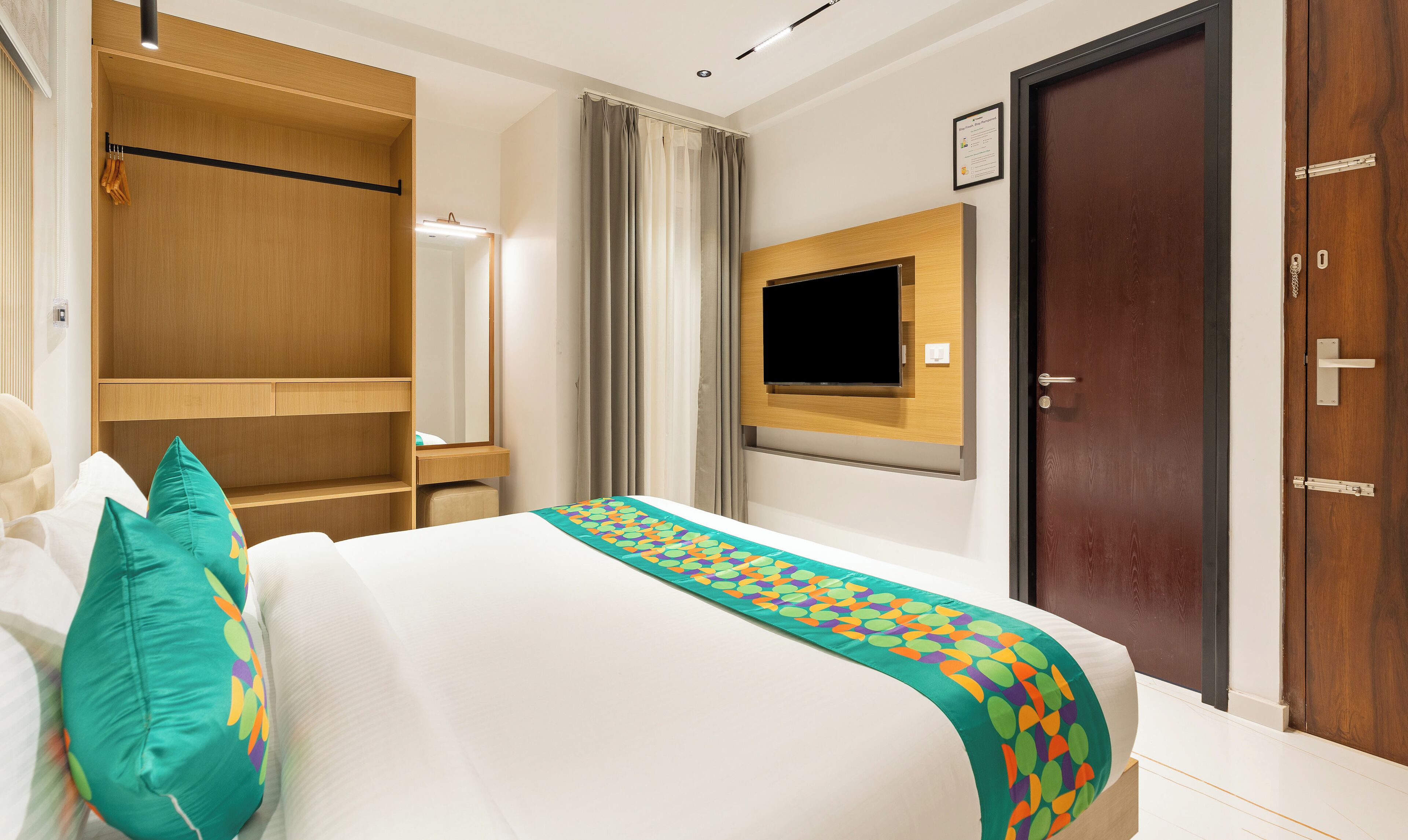 A hotel room with a bed, a wardrobe, a television, and a door.