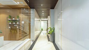 A modern hallway with a wooden panel wall, glass doors, and a marble floor. - Treebo Liyan Orchid, Hsr Layout (Bengaluru)