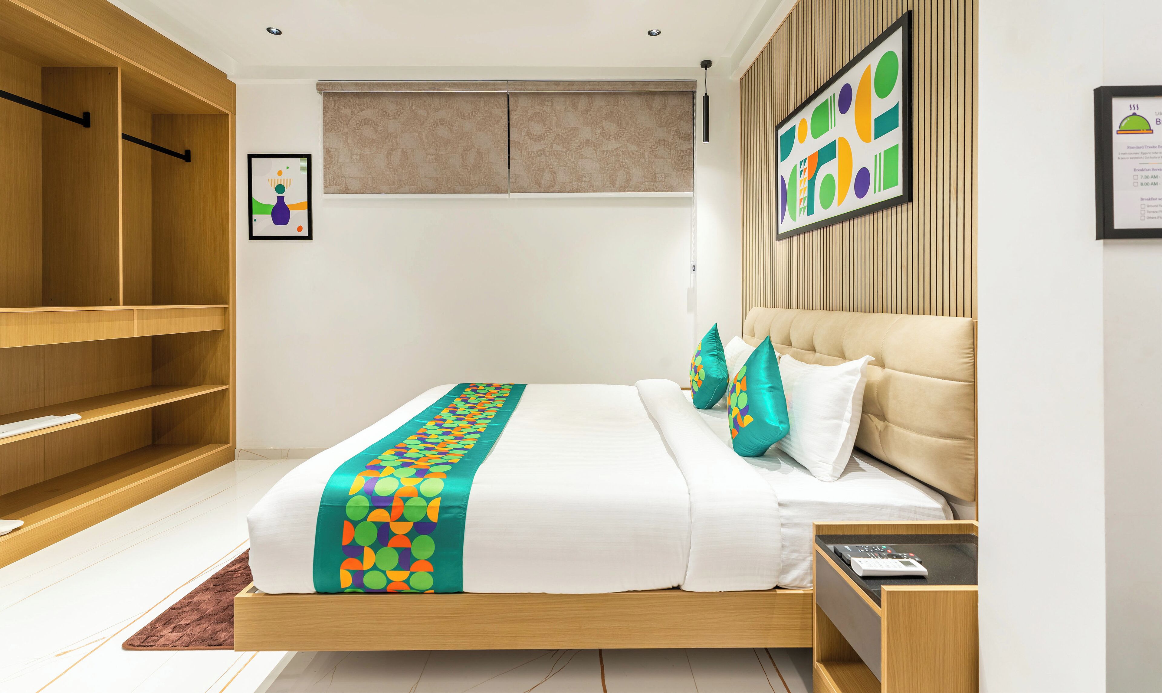 A modern hotel room with a wooden bed, a headboard with a geometric pattern, a bedside table, and a wardrobe.