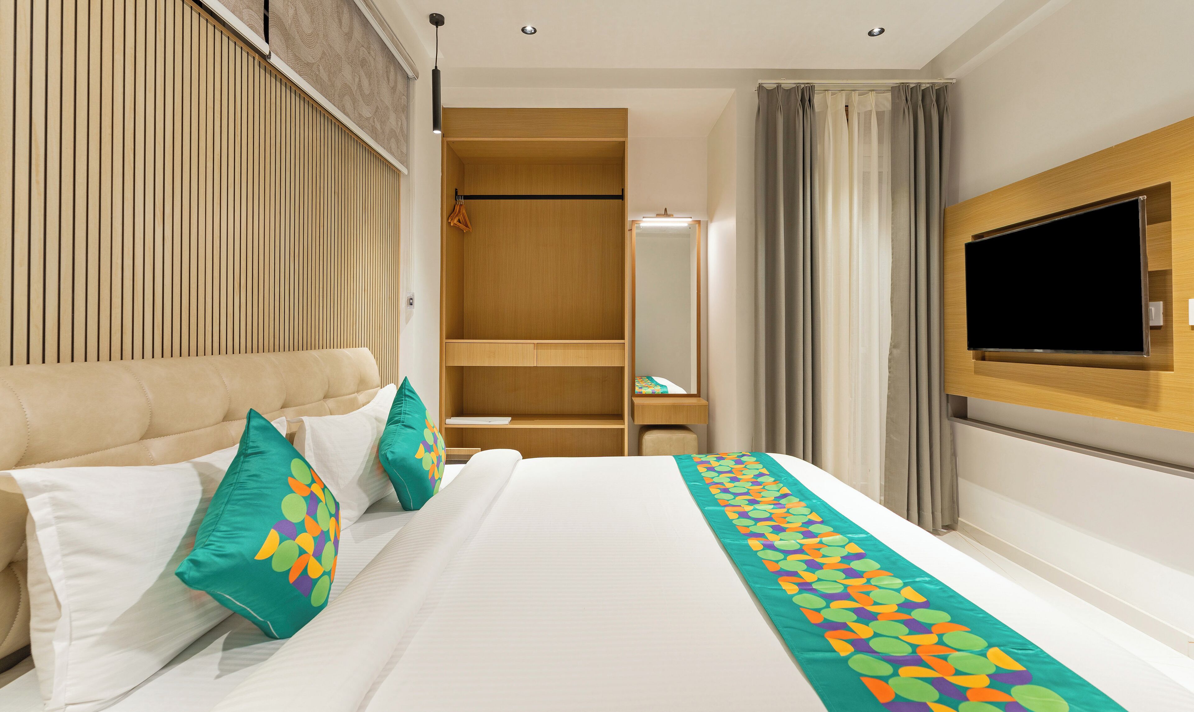 Une chambre d’hôtel avec un lit, une armoire en bois, un téléviseur fixé au mur et une salle de bain visible à travers une porte en verre.