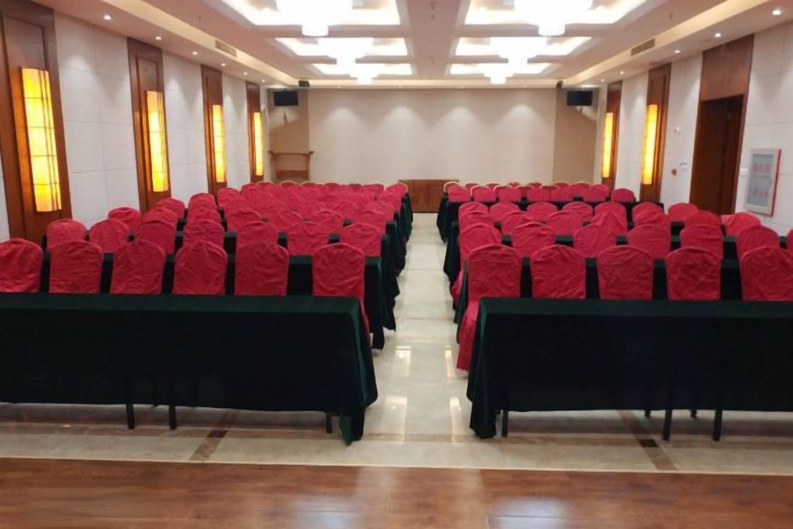 Une salle de conférence avec des rangées de tables et de chaises, un sol ciré et un plafond haut doté d’un éclairage encastré.