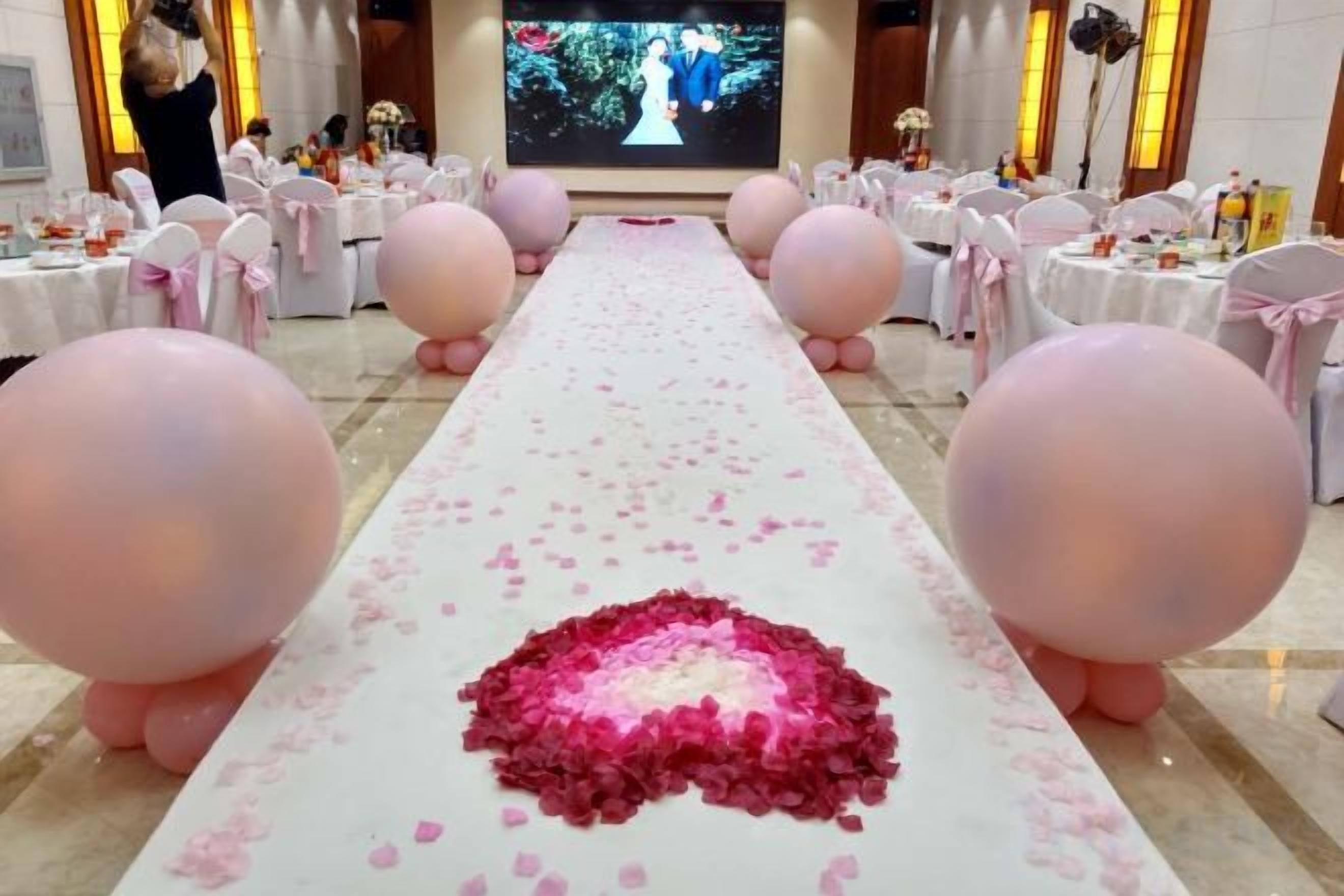 A long table with a white tablecloth, pink balloons, and rose petals arranged in the center.
