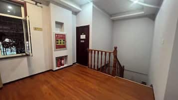 A hallway with wooden flooring, a staircase, and a fire safety poster on the wall.
