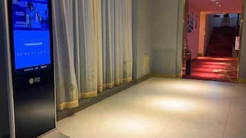 A hotel corridor with a digital display, a red carpeted staircase, and a curtain.