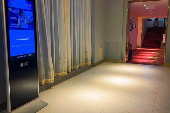 Un couloir d’hôtel avec un écran numérique, un escalier recouvert de moquette rouge et un rideau.