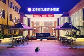 A hotel entrance with a sign, outdoor seating area, and a small garden. - Gong Mei Blue Peacock Business Hotel (Beijing Xisanqi) (Beijing)