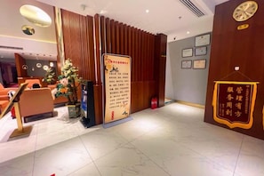 Un hall de hotel con una recepción, un árbol de Navidad y una pared con diplomas enmarcados.
