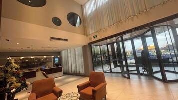 A hotel lobby with a reception desk, seating area, and large windows.