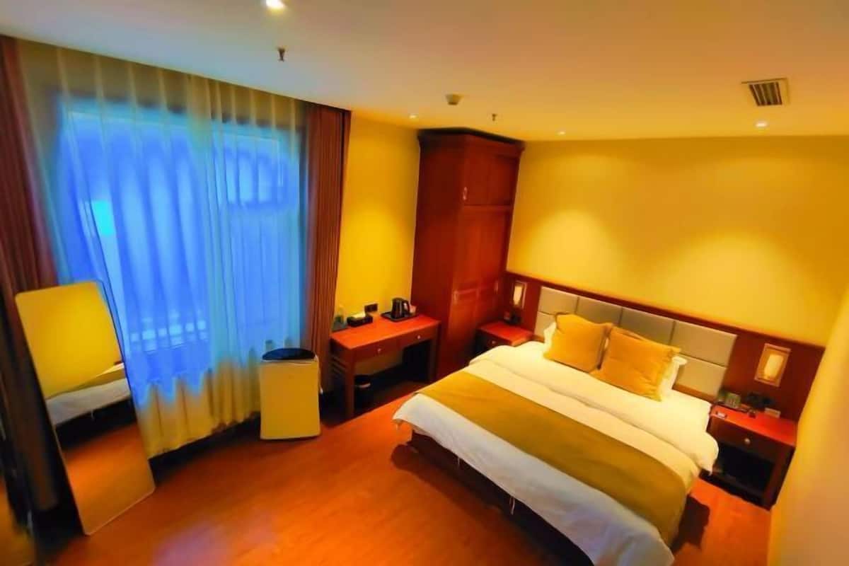 Habitación de hotel con una cama grande, un escritorio, una silla y un ventanal con cortinas.