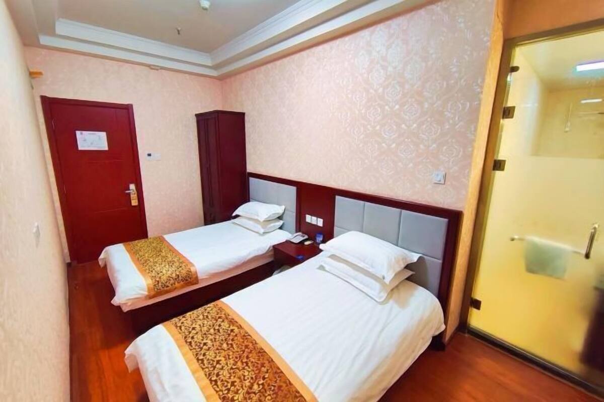 Habitación de hotel con dos camas, un armario de madera, una puerta roja y un papel tapiz estampado.