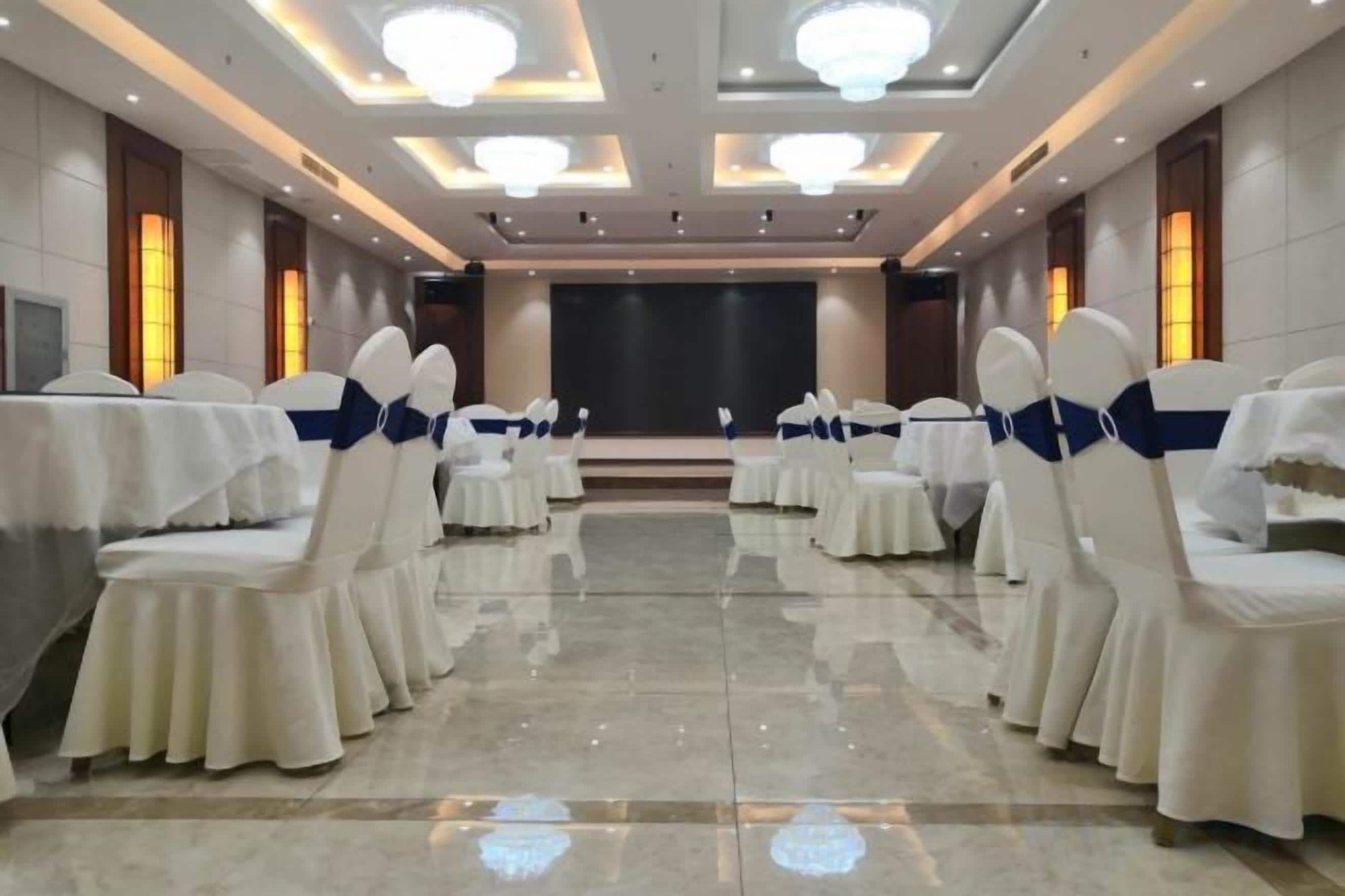 Un salón de conferencias con mesas y sillas redondas, un escenario y una pantalla de proyector.
