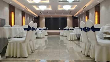 Un salón de conferencias con mesas y sillas redondas, un escenario y una pantalla de proyector.