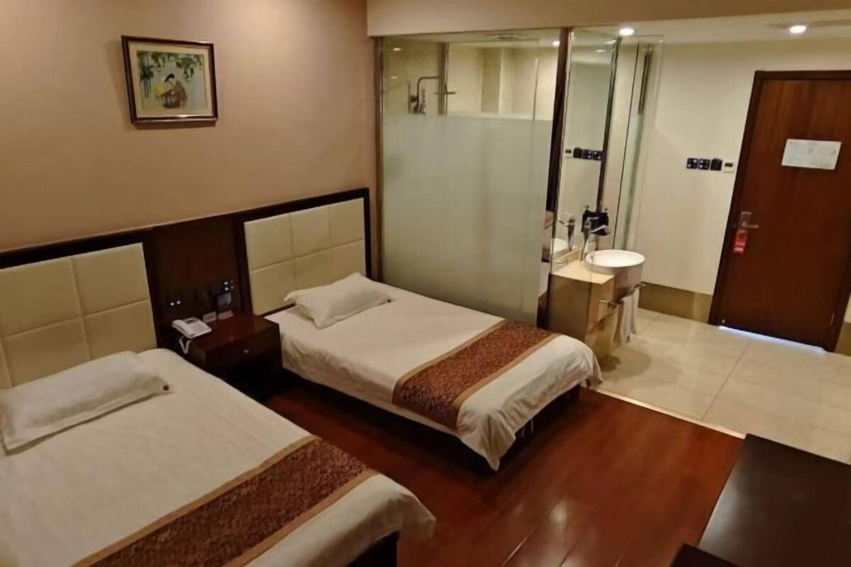 Habitación de hotel con dos camas, un baño con espejo y suelo de madera.
