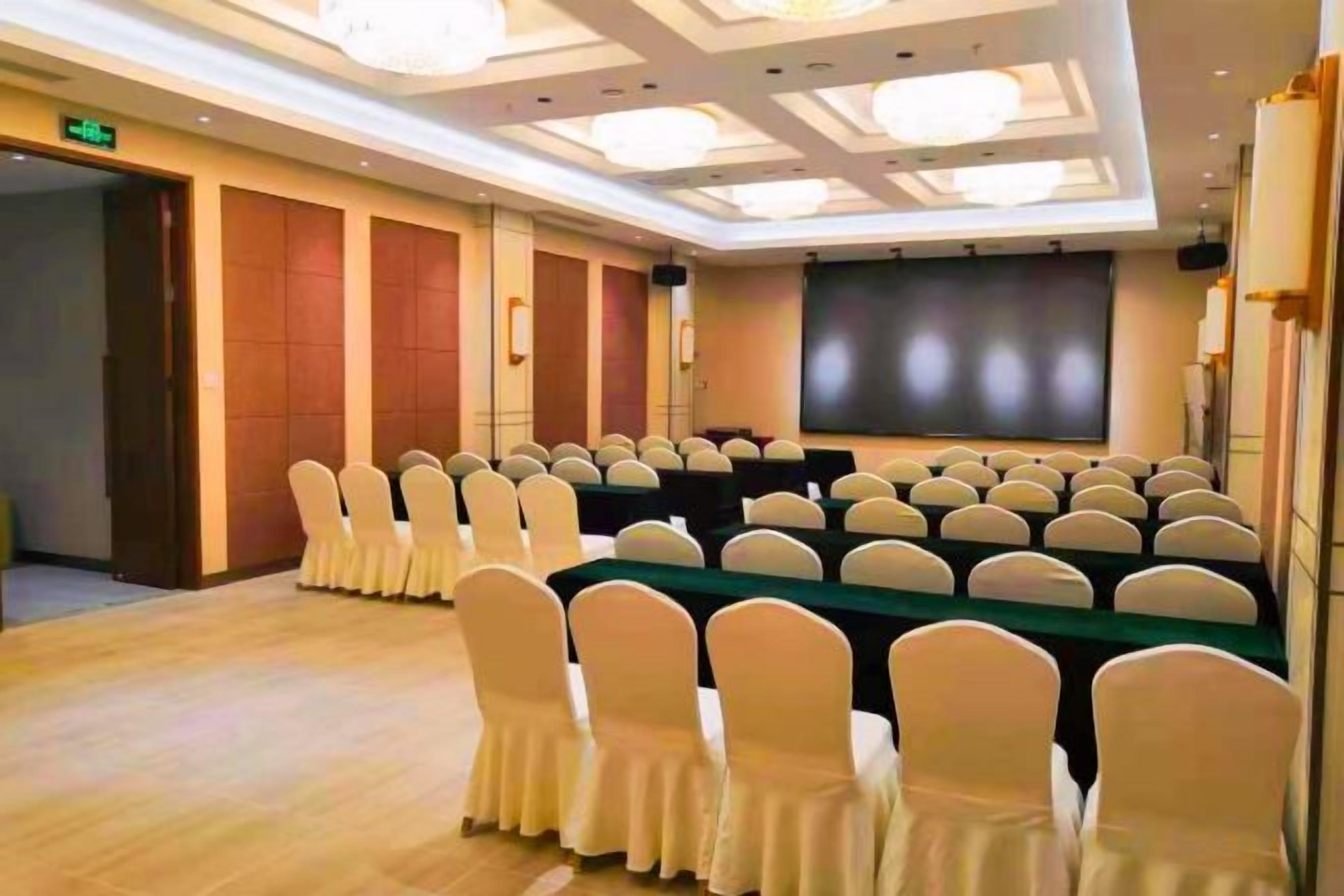 A conference room with rows of chairs, a long table, and a projection screen.