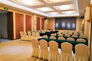 Une salle de conférence avec des rangées de chaises, une longue table et un écran de projection.