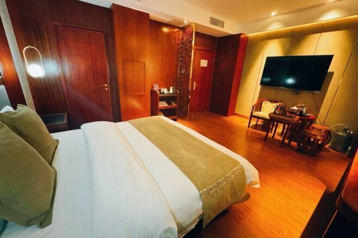 Habitación de hotel con una cama grande, un televisor montado en la pared, un armario de madera y una pequeña mesa con una silla.