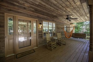 A wooden porch with a ceiling fan, a hammock, and two rocking chairs.