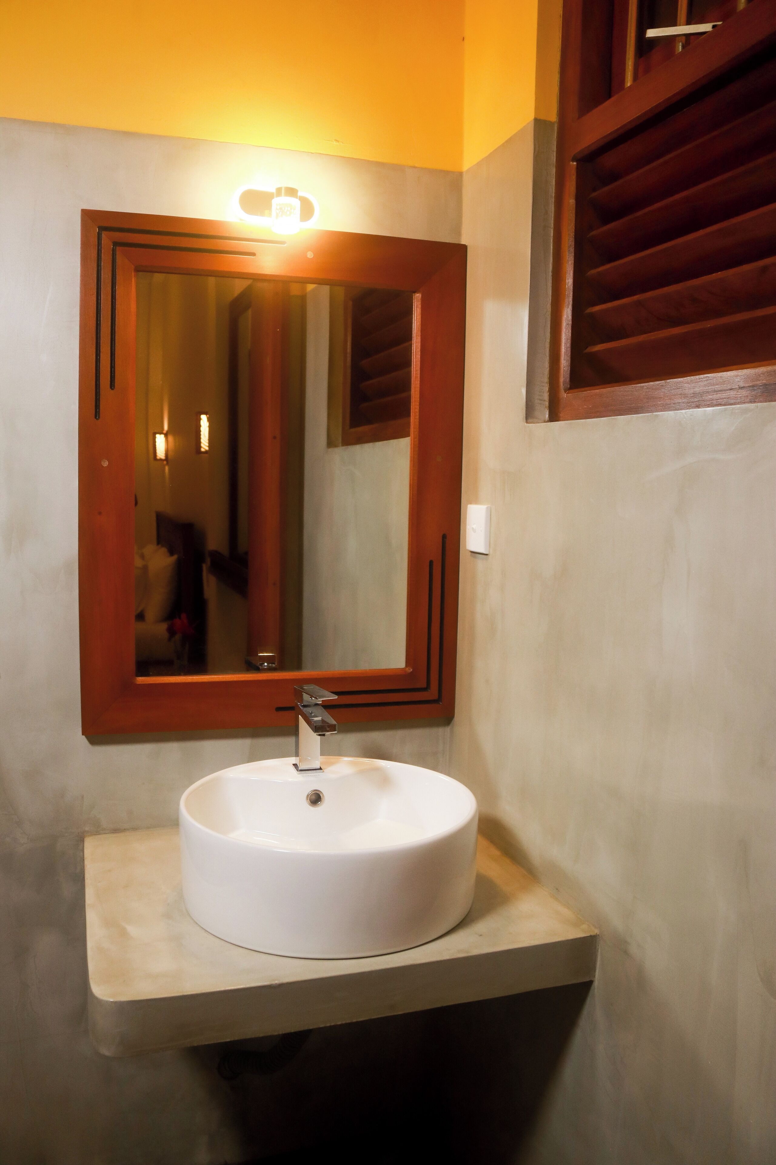 A bathroom with a white sink, a wooden-framed mirror, and a light fixture above the mirror.