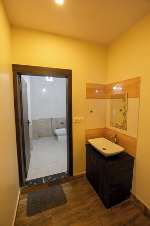 A bathroom with a wooden vanity, a mirror, and a door leading to a shower area. - Veda Resort (Udaipur)