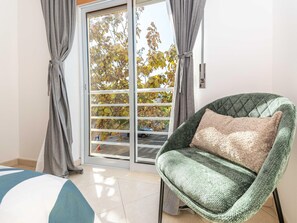 A room with a sliding glass door, a green patterned armchair with a beige pillow, and a blue and white striped rug. - Apartamento Azura in Concei o de Tavira (Tavira)