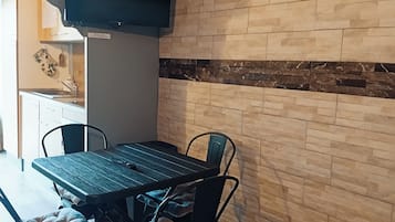 Un coin repas avec une table et des chaises, un téléviseur à écran plat fixé au mur et un coussin à motifs posé sur le sol.