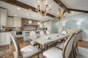 A spacious kitchen with white cabinetry, a large island, and a dining area with a wooden table and chairs. - 121 Breakwater Reach, Cape Shores (Lewes)